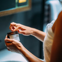 Frau im Badezimmer entnimmt Balsam aus Tiegel