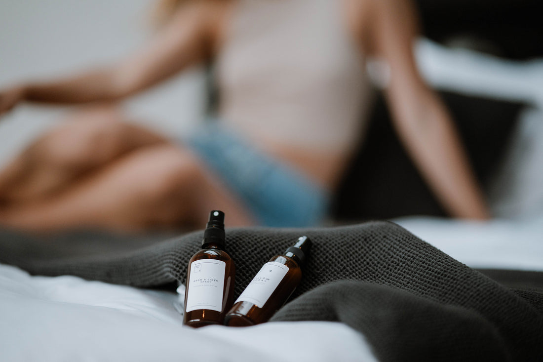 Das Kissenspray und das Raumspray liegen auf Bettdecke