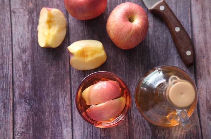 Äpfel und eine Essigflasche auf einem Holzbrettchen