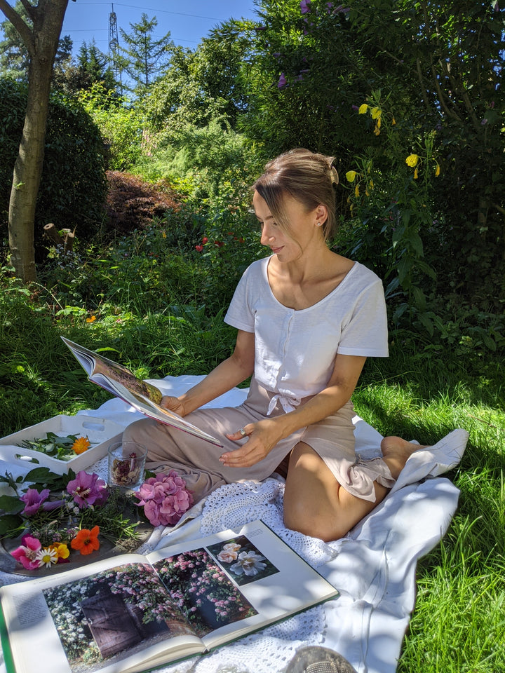 Frau sitzt auf einer Decke im Garten und liest ein Buch